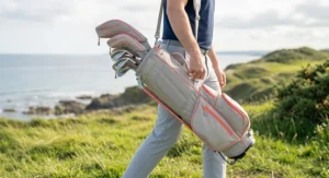 A close-up side view of a golf carry bag, with the larger side and valuables pockets splayed open to show easy access for storing gear like a rangefinder, scorecards, and balls.