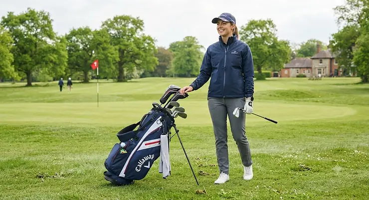 A beginner golfer standing on a British golf course holding a lightweight stand bag, ready for a round. golf bag for beginners