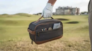 Golfer carrying a stylish golf shoe bag by its reinforced handle outside a traditional clubhouse.