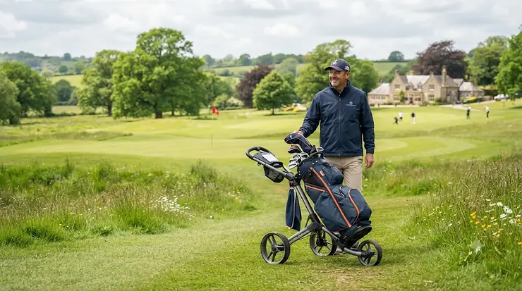 A golfer pushing a lightweight golf push trolley across a green fairway on a British golf course. lightweight golf push trolley