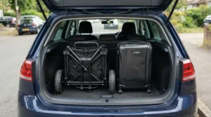 A compact push golf trolley for travel folded neatly inside a hatchback car boot alongside luggage